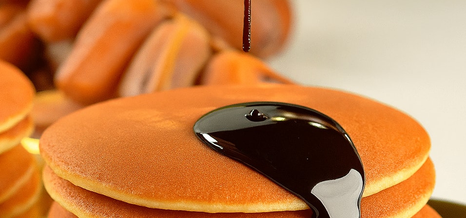 Date syrup being poured onto a stack of pancakes with a pile of dates behind